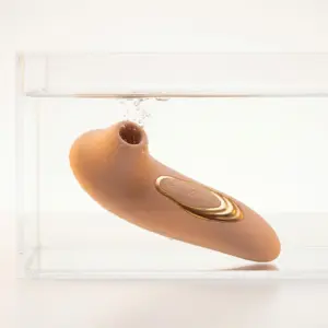 Suction Seduction mini clit suction stim in nude color submerged in water, showcasing waterproof design with curved ergonomic shape and gold control panel