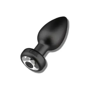 Angled close-up of the remote controlled butt plug, showcasing its smooth matte black finish, slender neck, and jewel-style power button on the base.