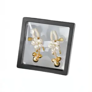 A pair of pearl-accented gold nipple clamps with dangling bells, elegantly displayed in a black presentation box with a clear cover.