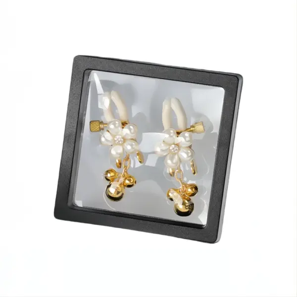 A pair of pearl-accented gold nipple clamps with dangling bells, elegantly displayed in a black presentation box with a clear cover.