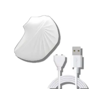 White suction cup vibrator with an elegant shell-like design shown next to its magnetic USB charger, highlighting its portability and discreet look.