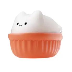 Front-on shot of the Kitty Swirl: a compact, white silicone cat figure with little ears and a simple “whisker” face, seated in an orange, ribbed silicone base.