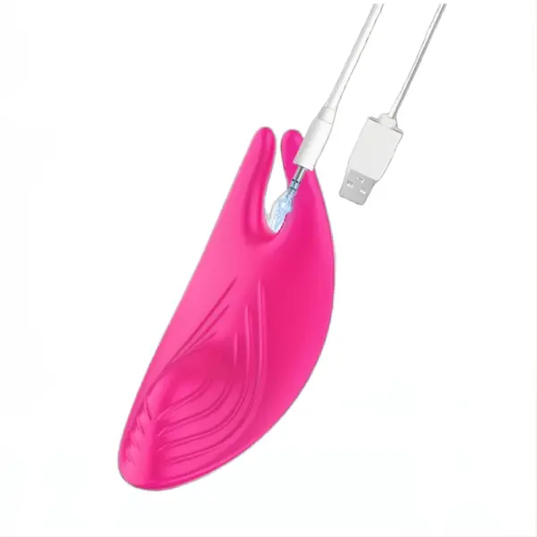 Close-up of the Rechargeable Vibrating Panty - Pink Secret showing a white USB cable being plugged into the charging port located between the dual tips, with a splash of water effect emphasizing waterproof design.