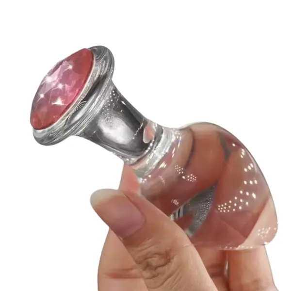 A hand holding the Crystal Clear Butt Plug – Clear Love, demonstrating its compact size, glossy glass finish, and pink crystal accent