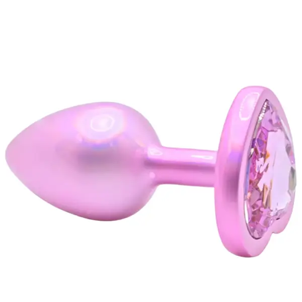 Glossy pink stainless steel butt plug with a tapered teardrop shaft and faceted heart-shaped pink jewel in its flared base, shown at an angle on a white background.