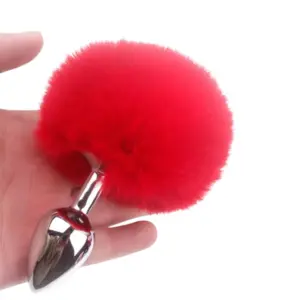 Hand holding the Flirtbud Rabbit Tail Metal Butt Plug showing the red tail pom-pom and smooth metal plug body