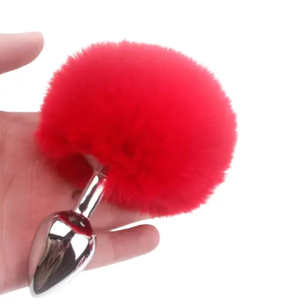 Hand holding the Flirtbud Rabbit Tail Metal Butt Plug showing the red tail pom-pom and smooth metal plug body