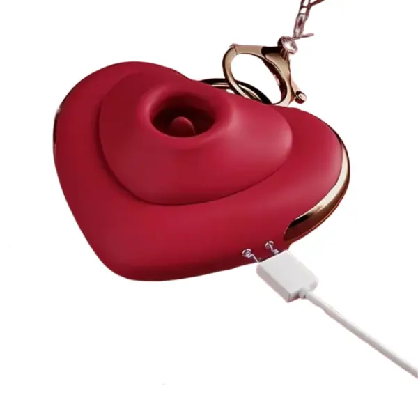 The Keychain Licking and Suction Vibrator - Heart Flutters shown mid-charge, connected via magnetic USB charging port, with emphasis on sleek red body and metallic detailing.