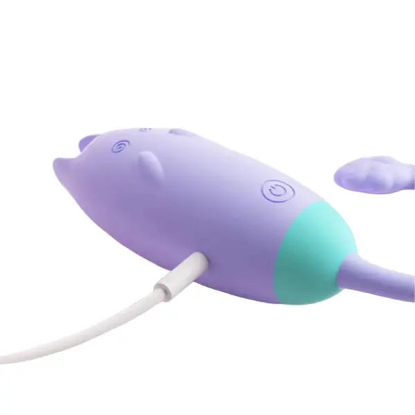 Side view of the Remote Control Kitty Love Egg – PurrVibes while charging via a USB cable, highlighting the silicone charging port and ergonomic form.