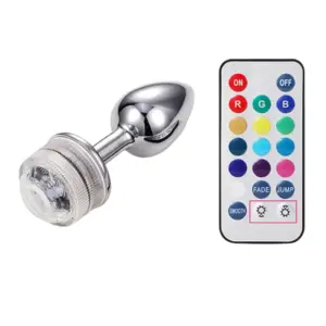 A metallic silver LED Light Butt Plug – Booty Glow with a clear light-up base and a color-changing remote control featuring 16 color buttons and lighting modes.