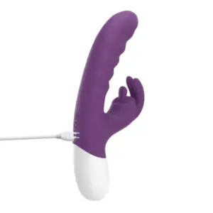 Close-up of the VoltBloom rabbit vibrator connected to a USB charging cable, showing the seamless purple silicone body and white plastic base.