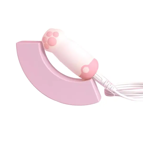 Cat paw love egg vibrator – Pawmé placed in a pink charging dock with a white USB cable connected, highlighting its charging setup and compact size.