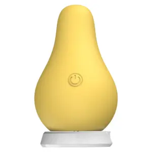 Pear Clit Vibrator – FruGasm in matte yellow silicone with a soft, rounded form and a central power button. Displayed upright on its white charging base.