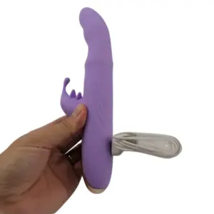 Hand holding the TapBun vibrator with white USB charging cable plugged in, showing flexible build and gold-tone base accent.